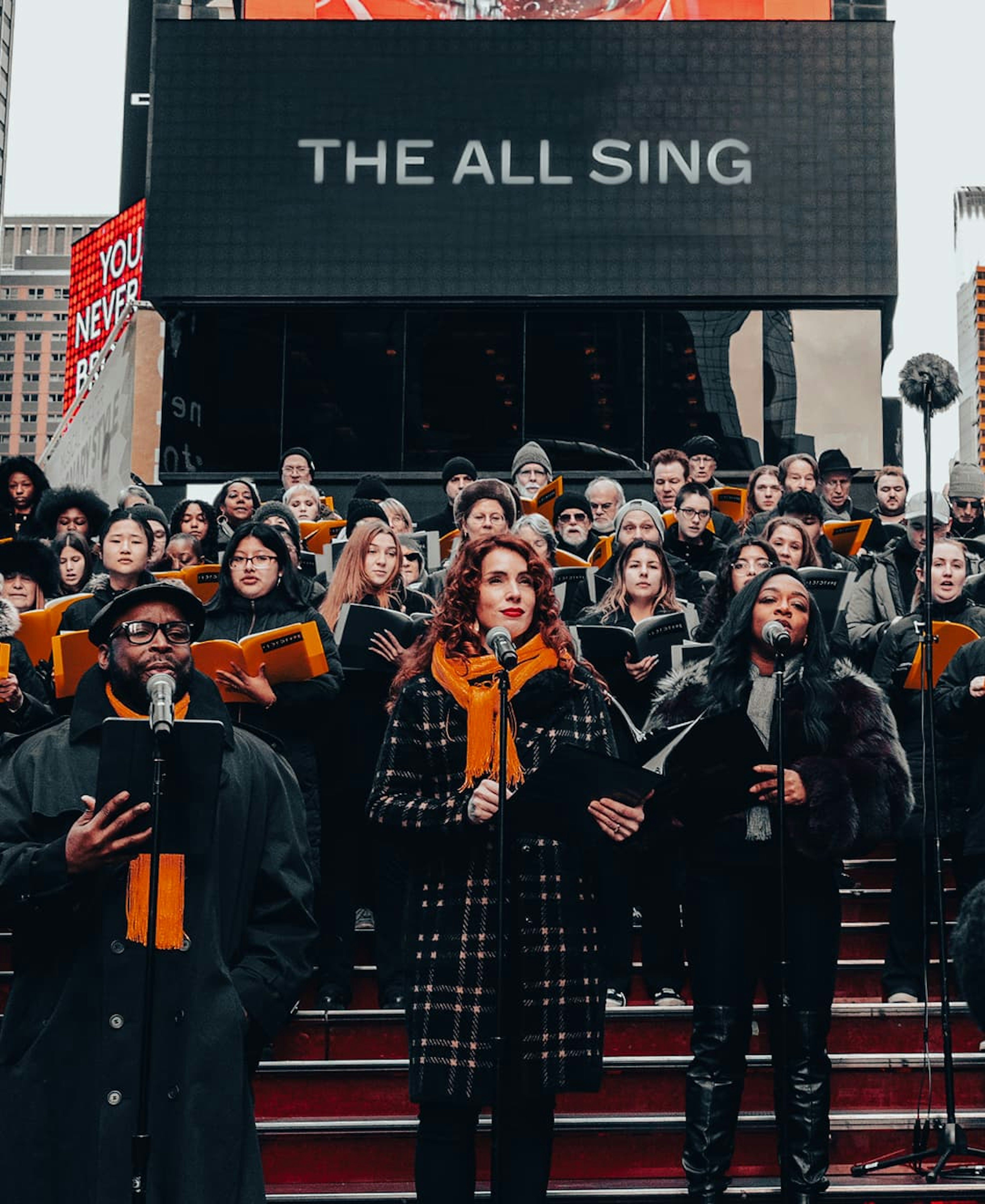 Picture of choir. The billboard behind them reads ‘THE ALL SING’